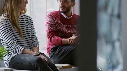 Two Young Adults Talking Together Indoors by Window