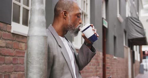 Man Drinking Coffee and Using Smart Phone on Street