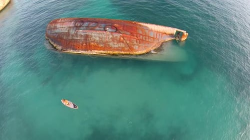 Aerial shot of young woman sup standup paddleboarding near a shipwreck in the Caribbean.
