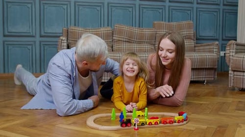 Family of Mother Father with Daughter Child Girl Riding Toy Train on Wooden Railway at Home Room