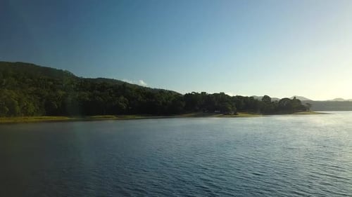 Drone footage flying over calm steamy lake (Tinaroo Dam) at sunrise towards a campsite on the bank.