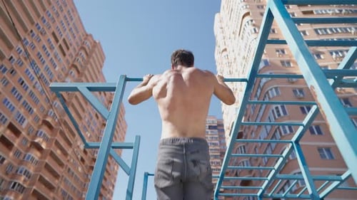 Athletic Man with Naked Torso Pulls Up on Horizontal Bar on Bright Sunny Day