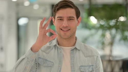 Man Gives Okay Sign, Smiling in Office