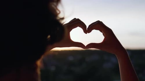 Woman Makes Heart Shape with Hands at Sunset
