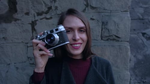 Woman Smiling Holding a Vintage Camera Near Brick Wall