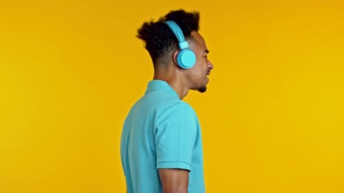 Handsome African Man Having Fun, Dancing with Blue Headphones in Yellow Studio. Music, Dance, Radio