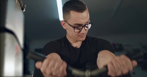 Man with Glasses Works Out with the Simulator to Pump Biceps and Triceps