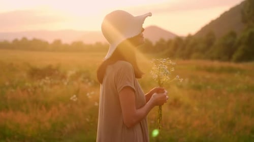 Woman with Flowers Standing in Sunlit Meadow