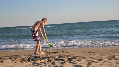 a Boy Digs Sand on the Beach with a Plastic Scoop or Shovel