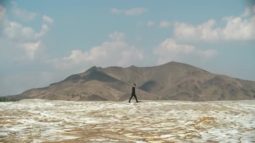 Man Walks Across Cracked Landscape Toward Mountains