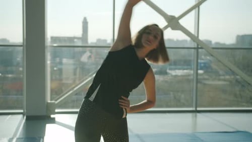 Young Female Athlete Bending Sidewards Training Alone in Modern Glass Wall Gym