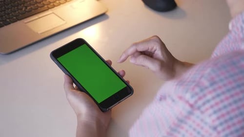 Over the shoulder shot of woman swiping on green screen mobile phone.