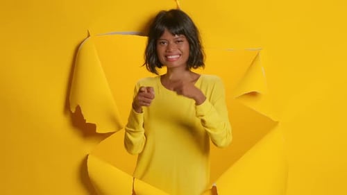Woman Points Through Torn Yellow Paper Background