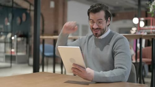 Young Man Celebrating Success on Tablet in Office