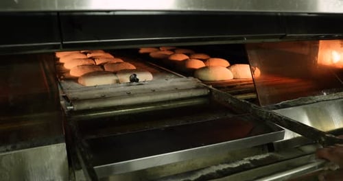 Ein Bäcker zieht manuell den Deck-Ofenlader und bewegt den rohen Brotteig in den Ofen - Bread Maki