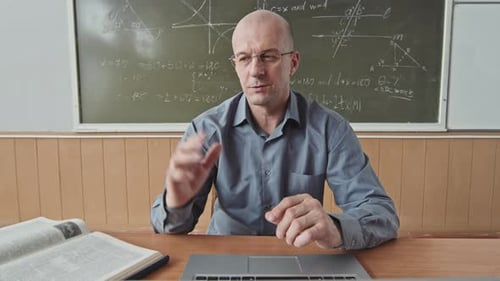 Teacher Explains Lesson at Desk in Classroom