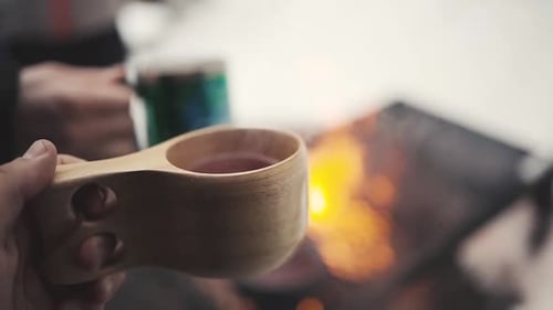 man holding a wooden cup with hot beverage in winter forest in Lemmenlaakso, Finland.