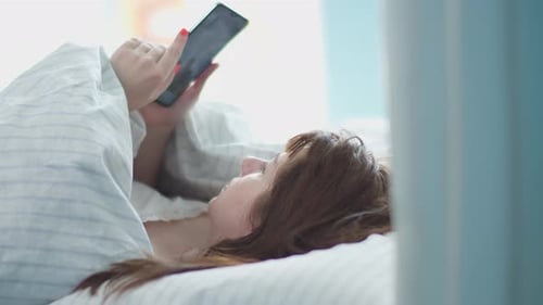 Woman Uses Smartphone in Bed in Bright Room