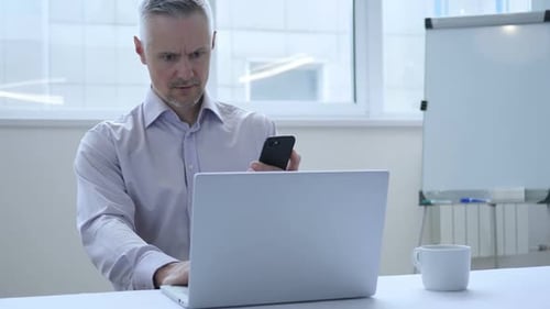 Man Working at Desk with Laptop and Phone