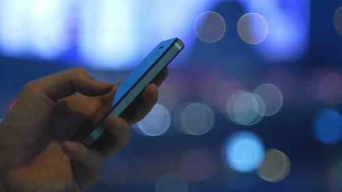 Hand Using Smartphone at Night with Bokeh Lights
