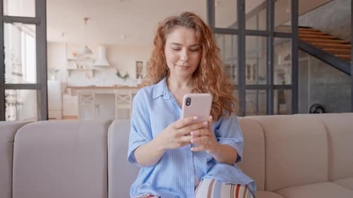 Woman Using Smartphone Relaxing on Sofa at Home