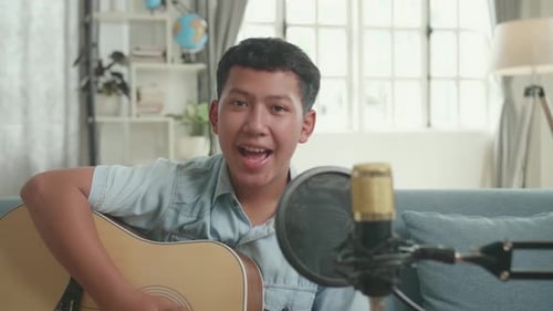Chico asiático con guitarra hablando con la cámara. El chico está transmitiendo