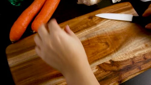 Woman's hands peeling fresh carrot above a wooden board close up