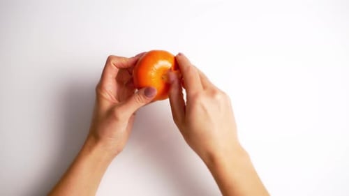 Hands Peeling a Fresh Tangerine on White