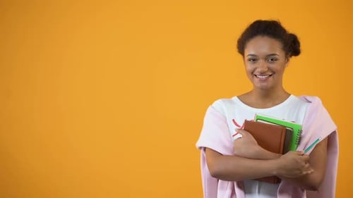 Smiling Young Woman Holding Books on Orange Background