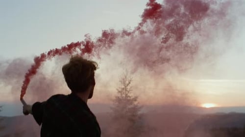 Adult Waving Red Smoke Flare on Mountain at Sunrise