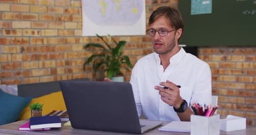 Caucasian male teacher teaching on videocall on laptop in the classroom at school