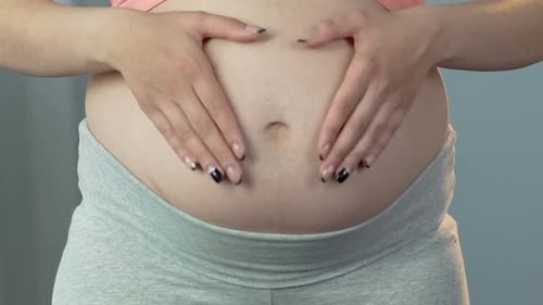 Femme enceinte caressant le ventre et mettant les mains en forme de cœur, gros plan