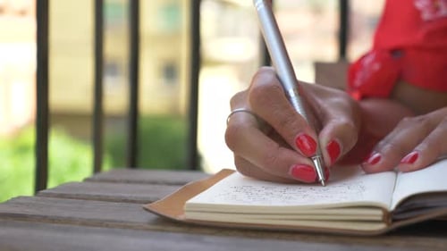 Close-up of a woman writing in a journal diary traveling in a luxury resort town in Italy, Europe.