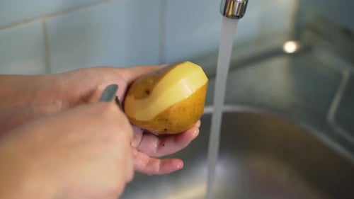 Peeling Potato Under Running Water in the Kitchen