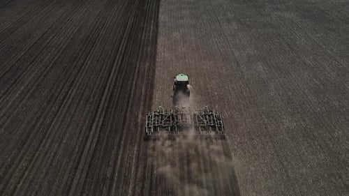Tractor with harrow system plowing ground on cultivated farm field, agriculture.