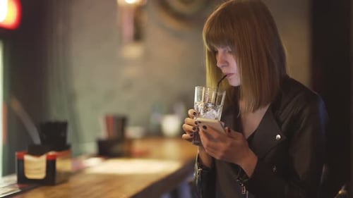 Young Beautiful Redhaired Woman Sitting in Cafe or Bar and Using a Smartphone