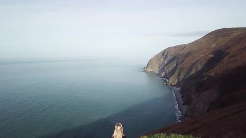 Overhead Drone Shot of Young Woman Sat on Edge of Coastal Cliff