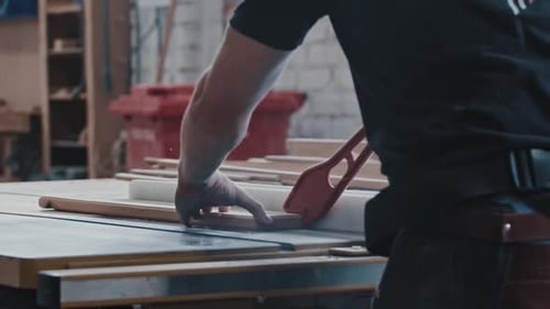 Carpentry Works Worker Slowly Cutting the Long Wooden Detail Using an Automatic Saw and Helping