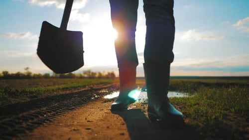 Farmer Walks With Shovel on Dirt Road at Sunrise