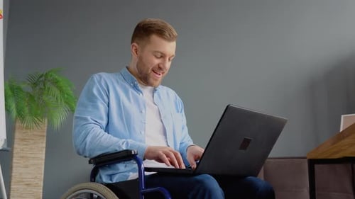 Handicapped Freelancer is Working with Laptop Typing Sitting in Wheelchair at Office