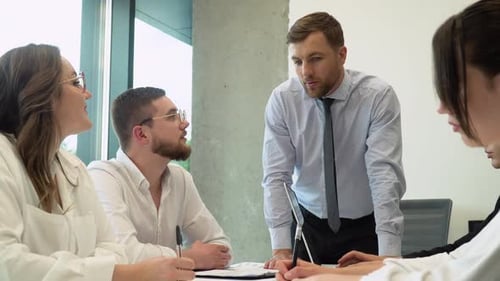 Teamleiter sitzt mit Kollegen am Tisch und diskutiert Arbeitsfragen bei Verhandlungstreffen