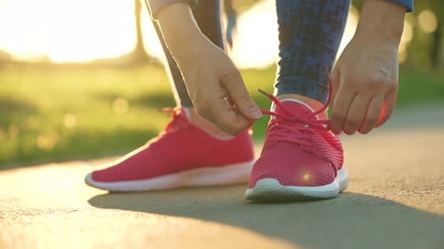 Woman Tying Shoelaces While Jogging or Walking at Sunset