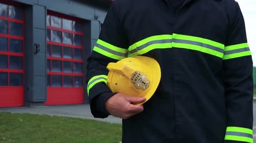 Ein Feuerwehrmann steht vor einer Feuerwache mit seinem Helm auf der Seite - Nahaufnahme