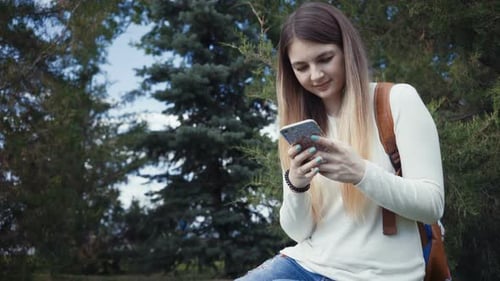 Footage Pretty Girl Sitting Near Tree in the Park and Using App on Her Smartphone