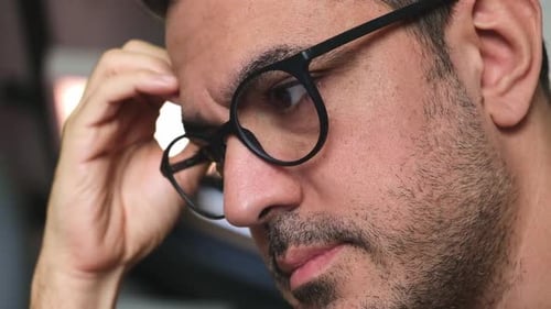 Nahaufnahme eines bärtigen Mannes, der durch eine Brille auf den Computerbildschirm schaut und liest, Augen bewegen sich