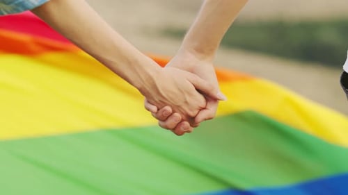 Couple Holding Hands in Front of Pride Flag