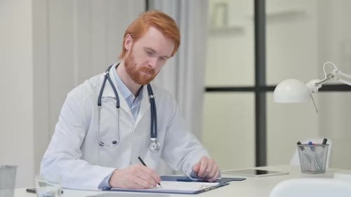 Rothaariger männlicher Arzt schreibt bei der Arbeit auf Papier