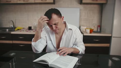 Male trader studying a book with charts sitting on the background of the kitchen