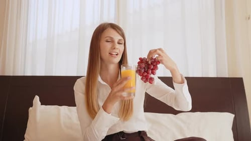 Pleasant Caucasian Woman Holding Glass of Fresh Juice and Grape in Hands and