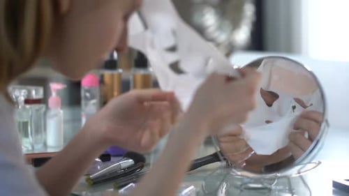 Young Woman Removing Facial Mask at Vanity Mirror
